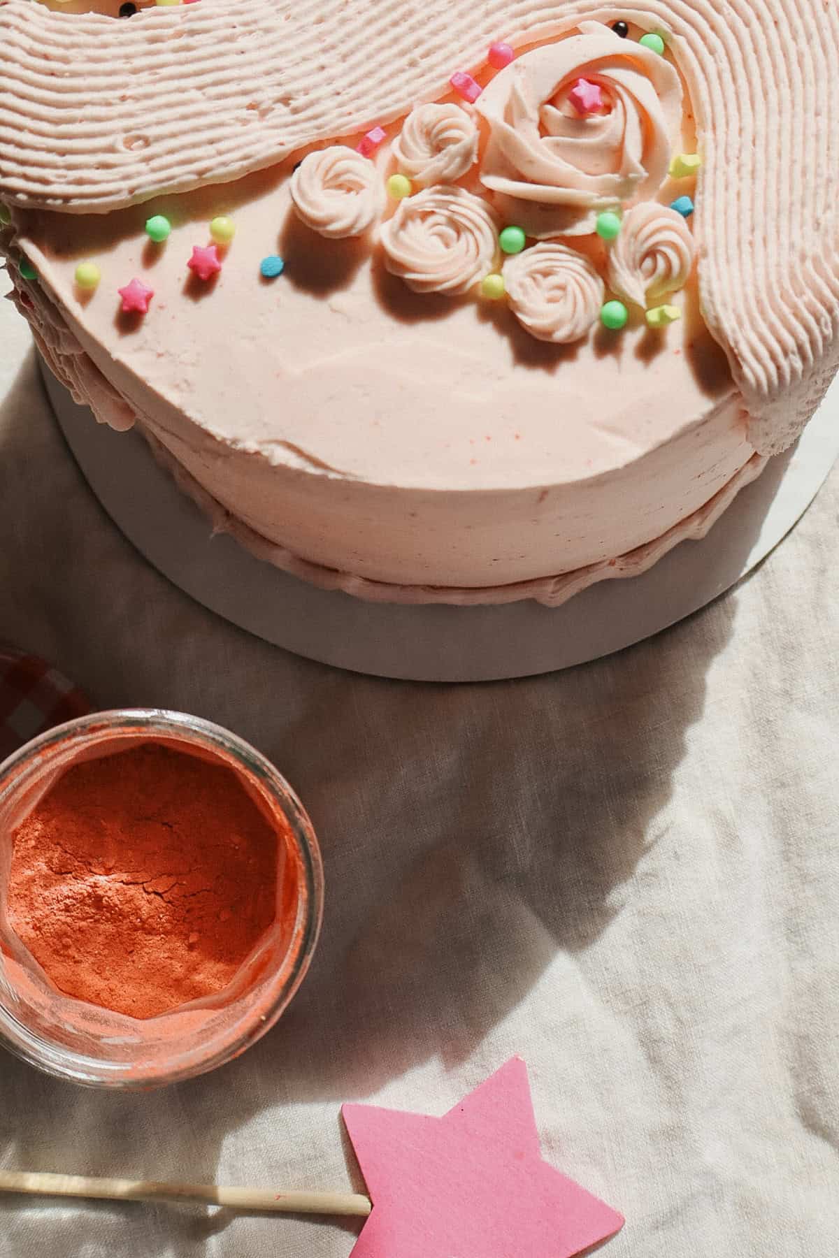 Strawberry Buttercream Frosting on a cake with a jar of freeze dried strawberries on a linen tablecloth with sunset lighting

