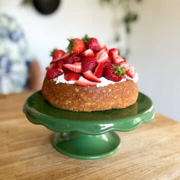 rustic shortcake cake on a vintage green cake stand sitting on a wooden butcher block counter with castiron skillets on the wall behind