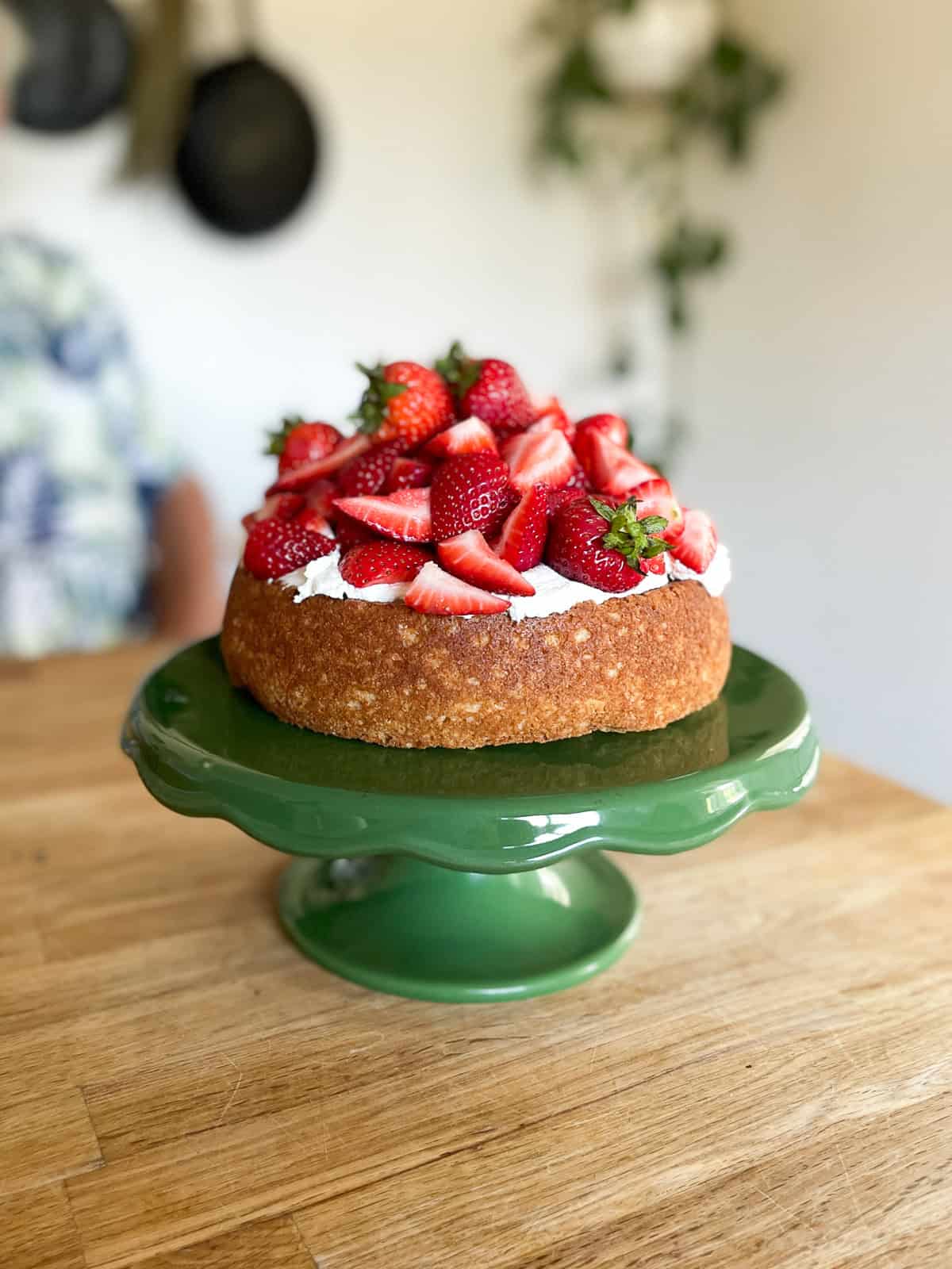 rustic shortcake cake on a vintage green cake stand sitting on a wooden butcher block counter with castiron skillets on the wall behind