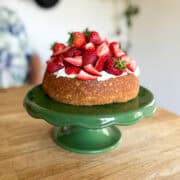 rustic shortcake cake on a vintage green cake stand sitting on a wooden butcher block counter with castiron skillets on the wall behind