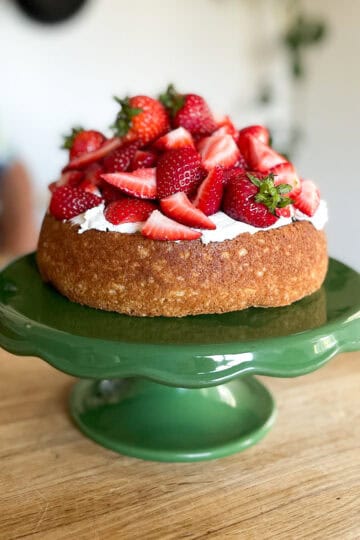 rustic shortcake cake on a vintage green cake stand sitting on a wooden butcher block counter with castiron skillets on the wall behind