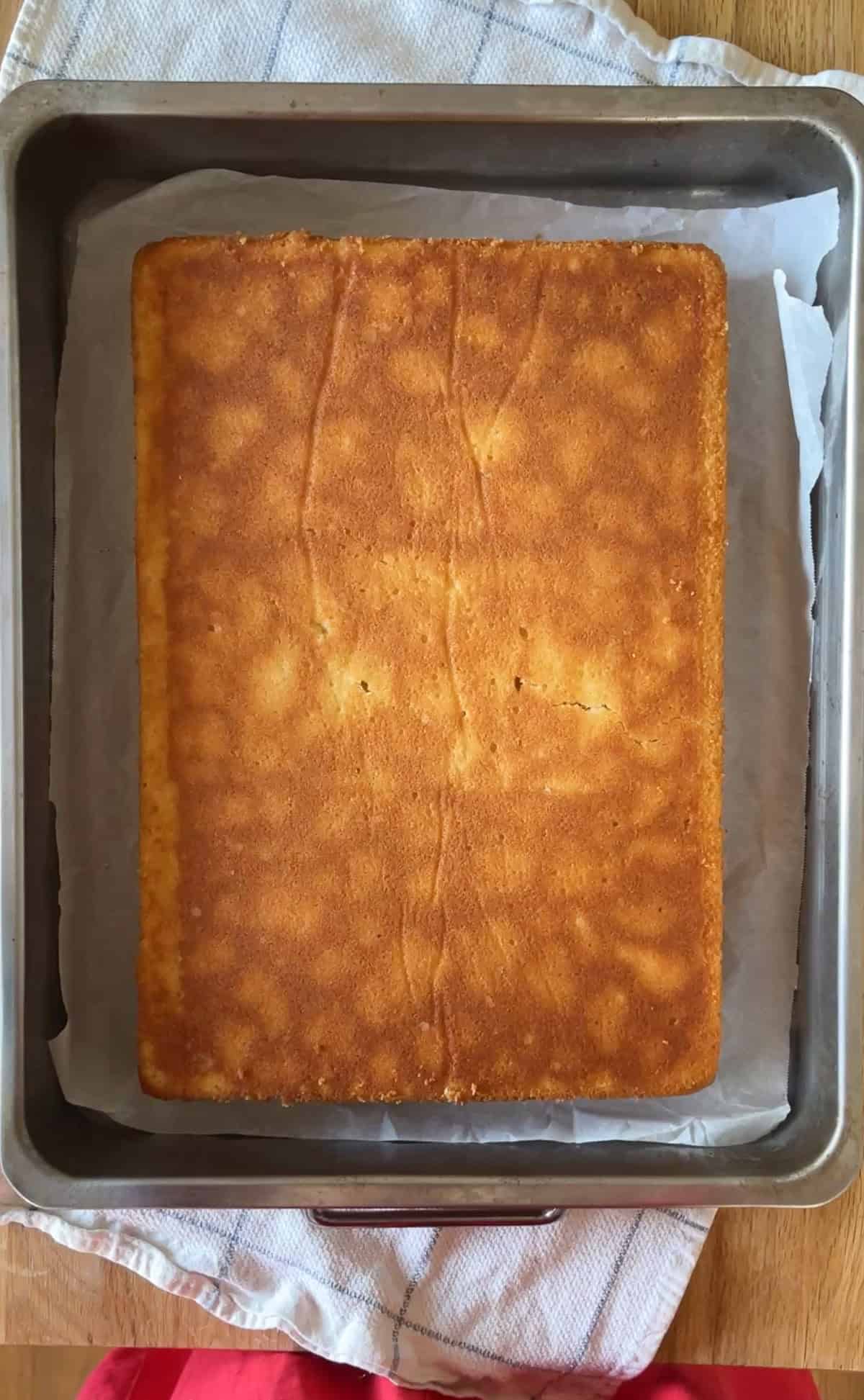 plain vanilla sheet cake in a rustic pan over a white with blue stripe kitchen towel on a butcher block