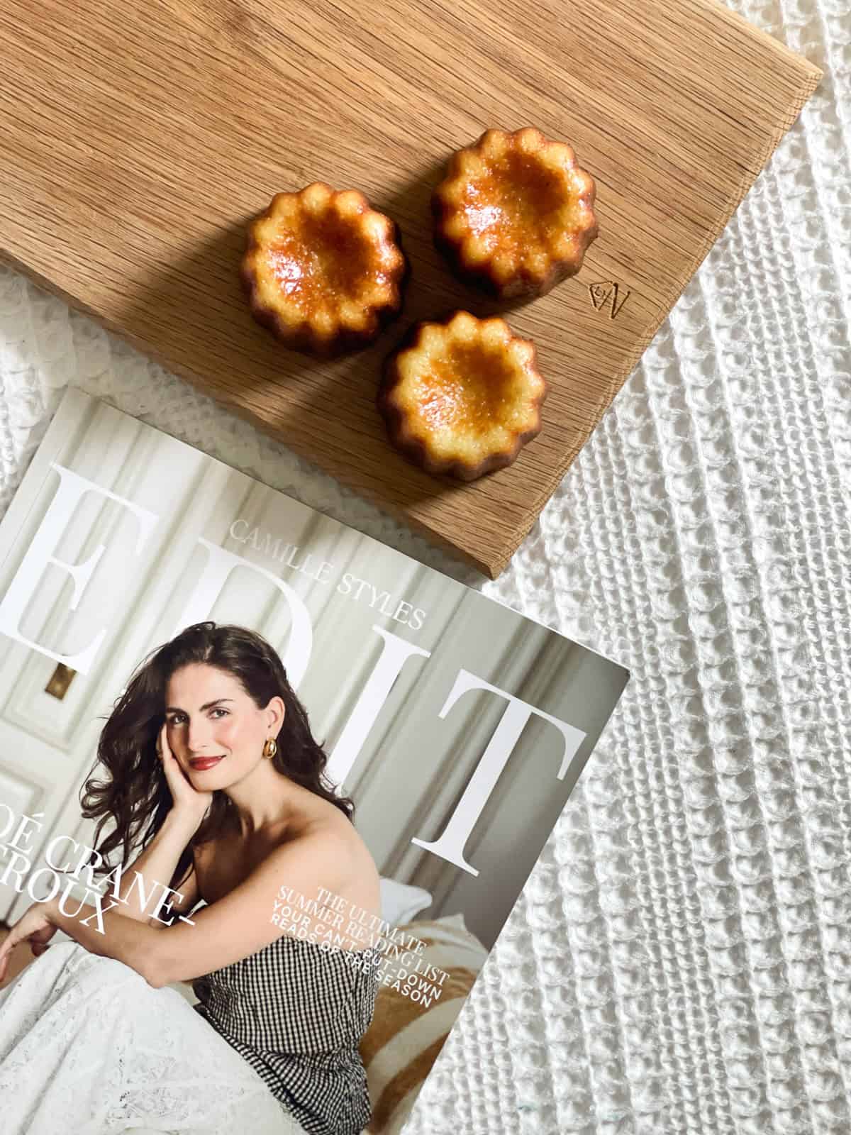 three canelés sitting on the casa zuma gathering board on a knit blanket with Camille style's EDIT magazine featuring Chloe Crane-Leroux.