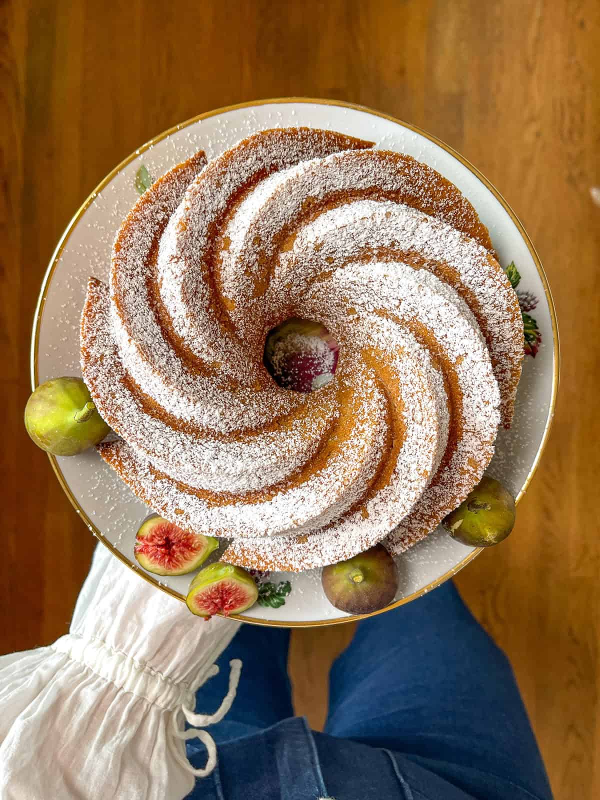 Golden spiced bundt snack cake dusted with powdered sugar on a white floral plate, garnished with fresh figs.