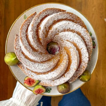 Golden spiced bundt snack cake dusted with powdered sugar on a white floral plate, garnished with fresh figs.