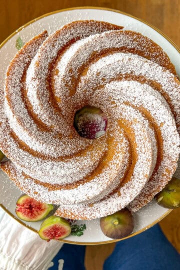 Golden spiced bundt snack cake dusted with powdered sugar on a white floral plate, garnished with fresh figs.